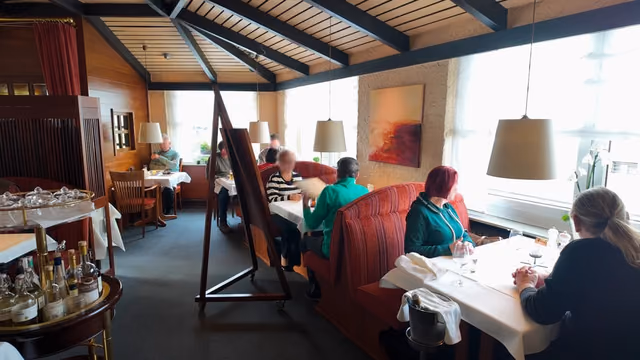 Dining room along the window front with daylight, red booth benches and a red wall painting