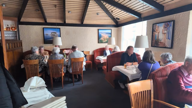 Wide view into the dining room of Restaurant Adria with its open roof truss and coastal pictures on the walls