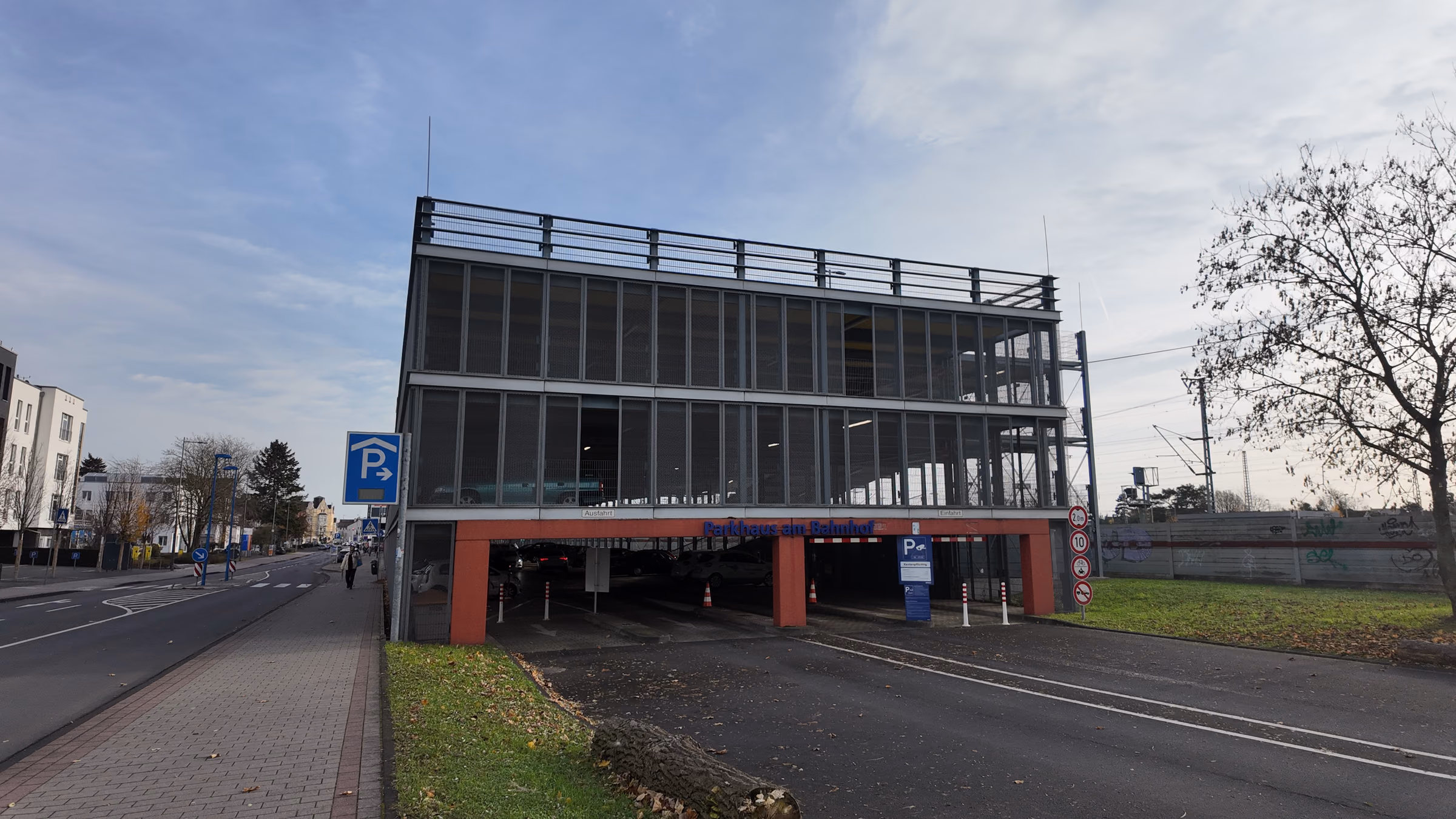 Street view of the multi-storey parking garage at the train station, with its red and blue sign and a blue P