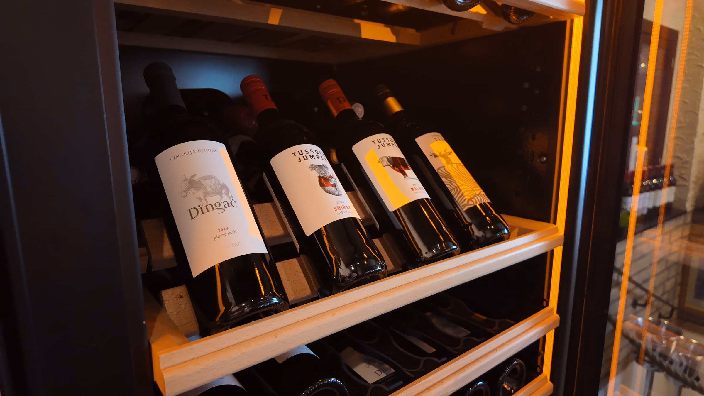 Red wine shelf in the illuminated wine fridge with several bottles lying side by side